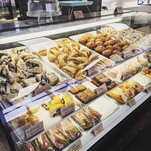 A display case filled with various baked goods, including pastries, cookies, and brownies, all labeled with names.