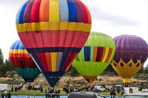 Colorful hot air balloons are inflated and ready for flight at a festival, with spectators gathered nearby.