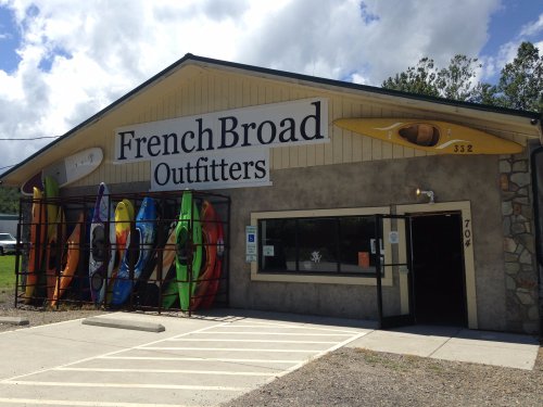 A storefront for French Broad Outfitters featuring colorful kayaks displayed outside and a welcoming entrance.