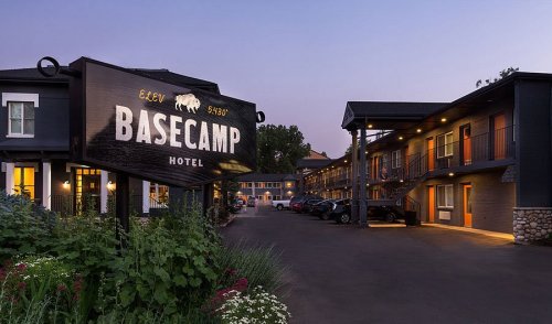 Sign for Basecamp Hotel at dusk, with a view of the building and parked cars surrounded by flowers.
