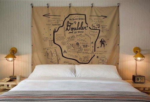 A cozy bedroom with a large map tapestry of Boulder above a bed, featuring warm lighting and a rustic design.