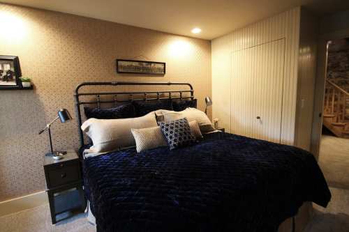 Cozy bedroom featuring a dark blue quilted bedspread, bedside lamp, and patterned wallpaper.