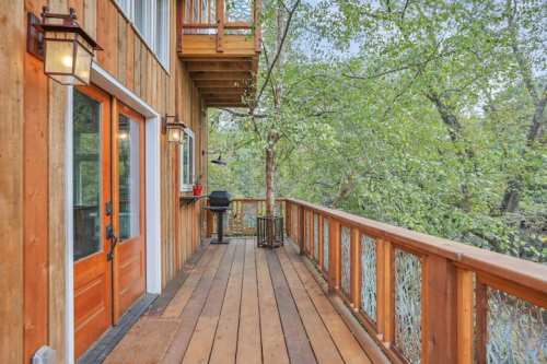 A wooden deck with lanterns, overlooking lush greenery and a grill, attached to a rustic wooden building.