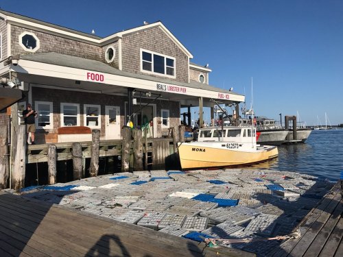 A yellow boat named "Mona" docked near a seafood restaurant on a sunny day, with lobster traps on the pier.