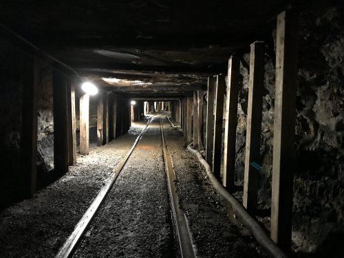 Dimly lit underground mine tunnel with wooden supports and railway tracks curving into the distance.