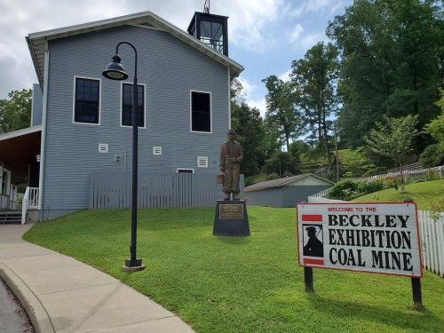 A statue of a miner stands in front of the Beckley Exhibition Coal Mine building and welcome sign.