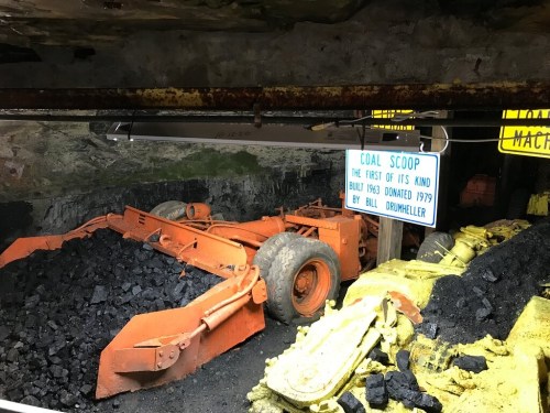 An underground coal mine display featuring orange coal scoops and a sign about their history.
