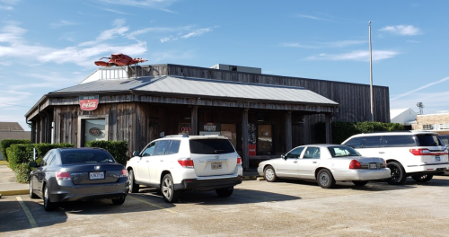 A wooden restaurant building with a metal roof, featuring a large crab sign, surrounded by parked cars.