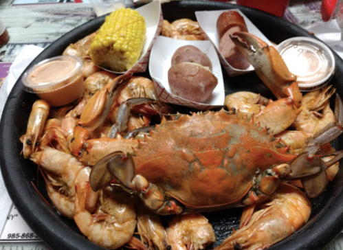 A platter of seafood featuring shrimp, a crab, corn on the cob, and potatoes, served with dipping sauces.