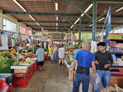 A bustling market scene with vendors and shoppers among colorful displays of fresh produce and goods.