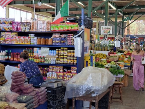 A vibrant market scene with shelves of packaged goods, fresh produce, and shoppers browsing among colorful displays.