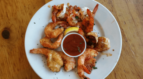 A plate of assorted shrimp, including fried and grilled, served with a lemon wedge and a side of cocktail sauce.