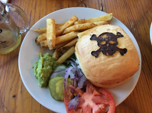 A plate with a burger featuring a skull and crossbones, served with fries, guacamole, and fresh vegetables.