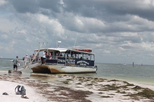 A boat docked on a sandy shore with passengers boarding, under a cloudy sky.