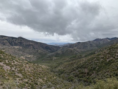 A panoramic view of a mountainous landscape under a cloudy sky, with lush greenery covering the hills and valleys.