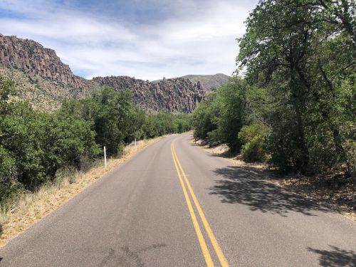 A winding road surrounded by lush greenery and rocky cliffs under a partly cloudy sky.