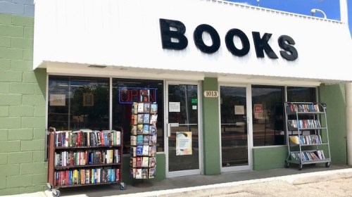 A bookstore with a large "BOOKS" sign, an open sign, and a display of books outside on a sunny day.