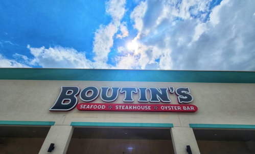 Sign for Boutin's Seafood Steakhouse Oyster Bar under a bright sky with clouds.