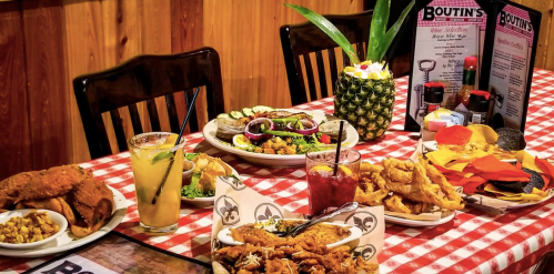 A table set with various dishes, including fried chicken, salads, and drinks, on a red and white checkered tablecloth.
