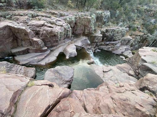 A rocky landscape with a small waterfall flowing into a serene pool surrounded by lush greenery.