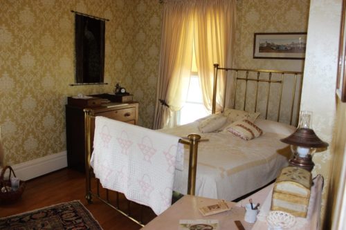 A vintage bedroom with a brass bed, patterned wallpaper, and soft natural light filtering through curtains.
