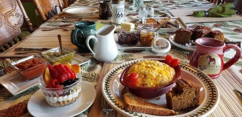 A beautifully set breakfast table with various dishes, including baked goods, fruit, and a savory egg dish.