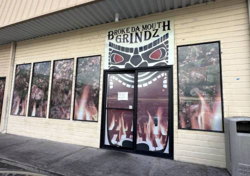 Entrance of "Broke Da Mouth Grindz" with a fiery design and large mask graphic on the door and windows.