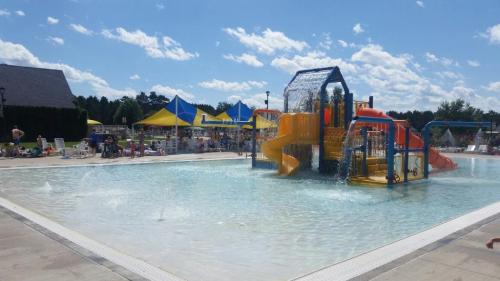 A sunny pool area featuring a colorful water play structure, slides, and lounge chairs under blue skies.