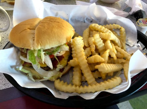 A hamburger with lettuce, tomato, and condiments, served with crinkle-cut fries on a tray.