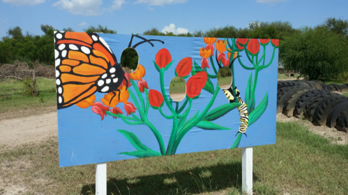 A colorful mural featuring a butterfly and caterpillar on a flower backdrop, with cut-out holes for photos.