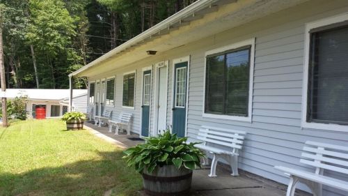A single-story building with blue doors, white benches, and planters, surrounded by greenery.