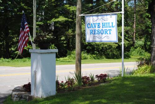 Sign for Cave Hill Resort with an American flag nearby, surrounded by greenery and flowers.