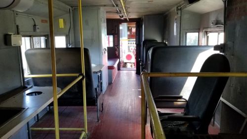 Interior of an old train car, featuring empty seats, a narrow aisle, and a view towards the entrance.