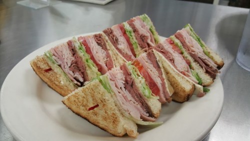 A plate of neatly sliced sandwiches with layers of turkey, roast beef, lettuce, and tomato on toasted bread.