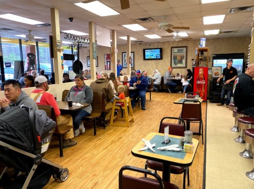 A busy diner with families and individuals seated at tables, enjoying meals in a casual, welcoming atmosphere.