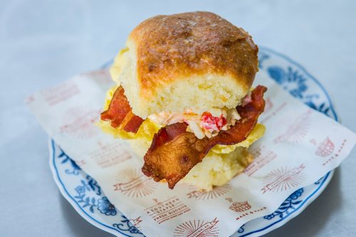 A delicious biscuit sandwich filled with crispy bacon and creamy filling, served on a decorative plate.