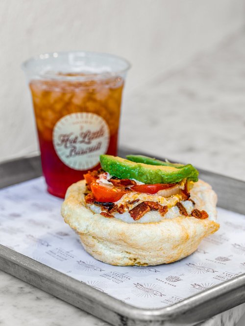 A savory pastry topped with bacon, tomato, and avocado, alongside a glass of iced tea on a tray.