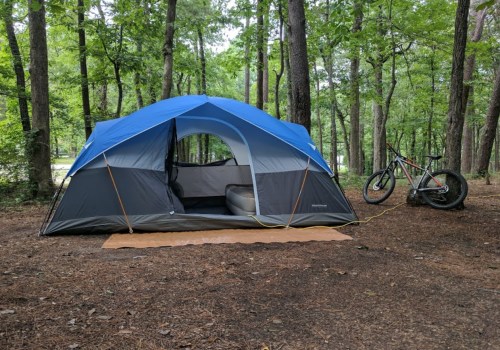 A blue and gray tent set up in a wooded area, with a bicycle parked nearby on the forest floor.