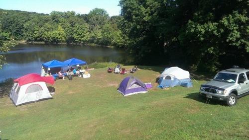 A scenic campsite by a pond, featuring tents, canopies, and people enjoying the outdoors.