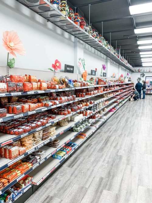 A grocery store aisle filled with colorful packaged goods and snacks, with decorative flowers on the shelves.