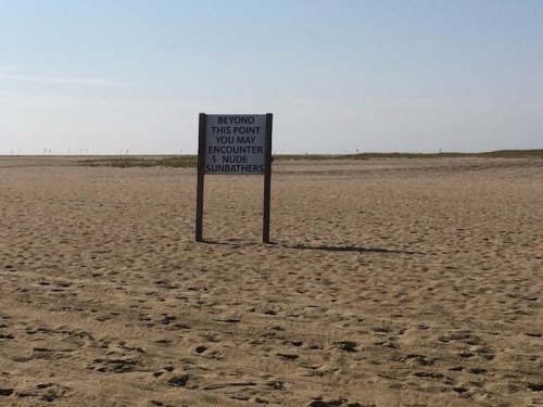 Sign on a sandy beach warning that nude sunbathers may be encountered beyond that point.