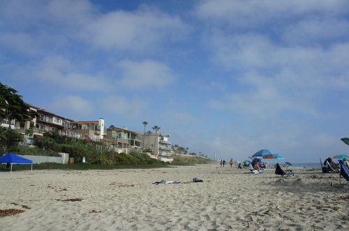 A sandy beach with umbrellas, people, and beachfront homes under a cloudy sky.