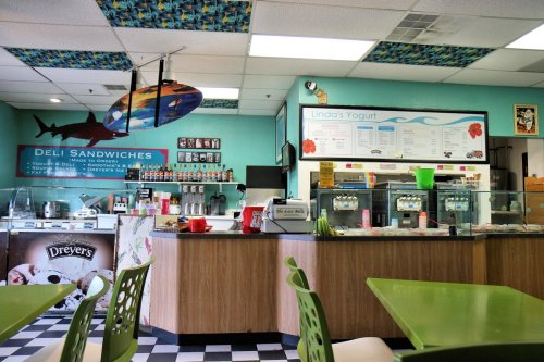 A colorful deli interior featuring a counter with sandwiches and yogurt, bright decor, and checkered flooring.