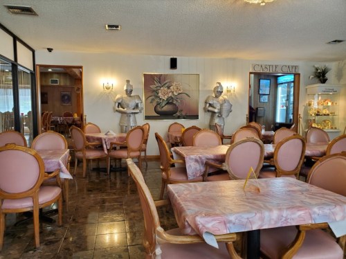 Interior of a restaurant with pink tables, chairs, and knight statues, creating a whimsical dining atmosphere.
