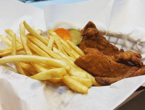 A basket of golden French fries and crispy fried fish fillets, served with pickles and a slice of carrot.
