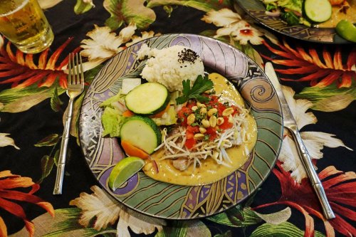 A colorful plate featuring rice, vegetables, and a creamy sauce with herbs, set on a floral tablecloth.