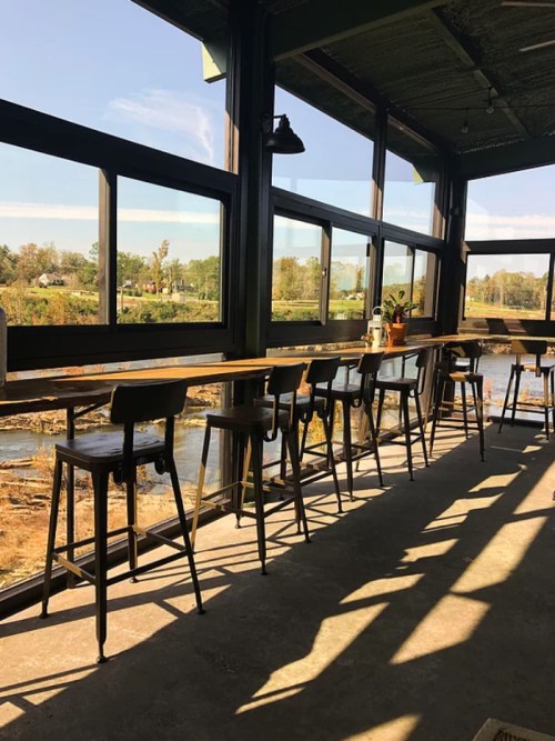 A bright, modern café interior with tall stools and large windows overlooking a scenic view.