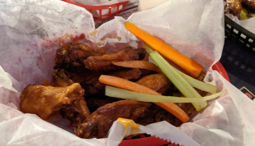 A basket of chicken wings with celery and carrot sticks, served on parchment paper.