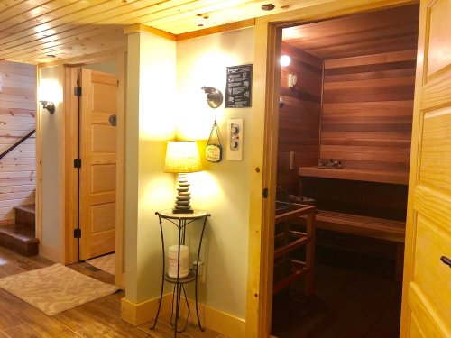 Cozy interior hallway with wooden walls, a lamp, and a sauna door on the right. Stairs visible in the background.
