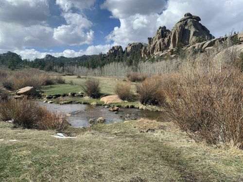 A serene landscape featuring a stream, rocky formations, and lush greenery under a partly cloudy sky.
